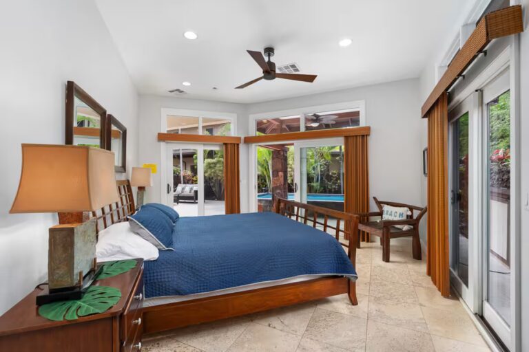 Bedroom with a blue bedspread opening onto the patio at Kona Luxury Estate