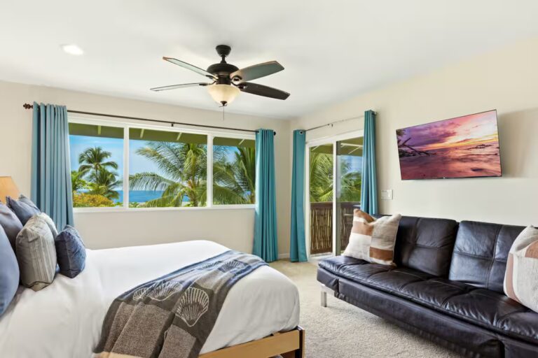 Bedroom with a sofa and windows overlooking palm trees at H12 Kona home