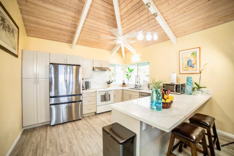 White kitchen with an island and stainless-steel refrigerator at H7 Kona home
