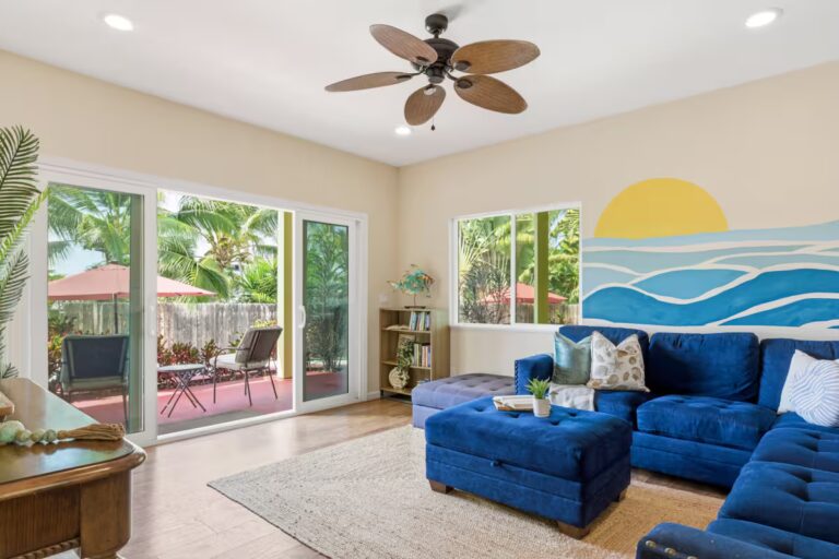 Blue sectional sofa beneath a painted ocean-and-sunset mural at H12 Kona home