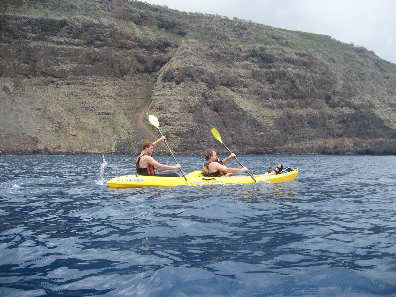 Kayaker on blue water at Kealakekua Bay with the coastal cliffs behind