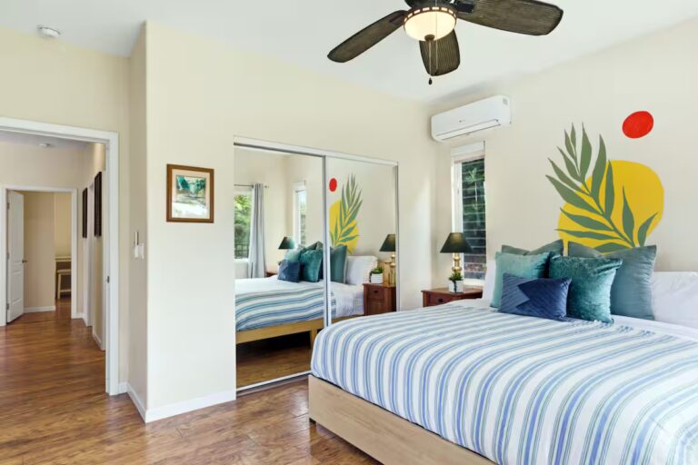 Bedroom with striped bedding and a tropical leaf mural at H12 Kona home